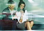 Businessman and businesswoman sitting together, looking at laptop