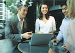 Professionals sitting at cafe table, talking over laptop