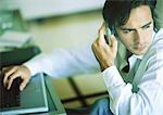 Man using laptop, phoning, looking over shoulder