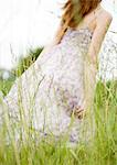 Jeune femme qui marche dans l'herbe, robe soufflant dans le vent