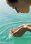 Woman leaning face over water, cupping water in hands