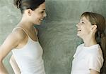 Two sisters standing, looking at each other and laughing, side view