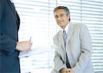 Businessman smiling at camera while colleague signs document