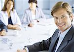 Businessman smiling, meeting in background, portrait