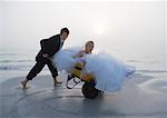 Groom pushing bride in wheelbarrow on beach