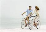 Mature couple riding bikes on beach