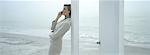 Woman leaning against doorframe on beach, using cell phone