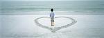 Boy standing inside heart drawn on beach, rear view