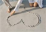 Woman drawing heart in sand on beach, partial view