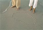 Couple standing by heart drawn in sand, view of knee down