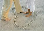 Woman standing in heart drawn in sand, man stepping into heart, view of knee down