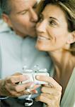 Mature couple with present, man kissing woman's cheek