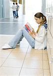 Jeune fille assise sur le sol dans le couloir de l'école, se penchant contre les casiers et étudier