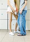 Teen boy and girl standing next to lockers, chest down