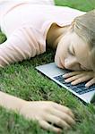 Teenage girl in grass, lying with head on laptop computer