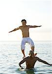 In sea, man standing on second man's shoulders is losing balance