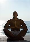 L'homme assis en posture d'yoga sur la plage, la silhouette