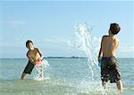 Two boys splashing in water at beach