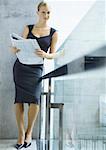 Businesswoman leaning on railing, smiling at camera, full length