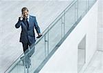 Businessman leaning on railing, using cell phone, high angle view