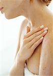 Young woman applying moisturizer to shoulder