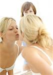 Two young women, one kissing reflection in mirror