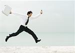 Businessman running and jumping on beach
