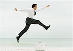 Businessman on beach, jumping over briefcase