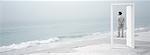 On beach, man seen through open doorway, looking at view