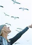 Young woman feeding seagulls in sky