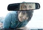 Woman lying on hood of car, looking through windshield