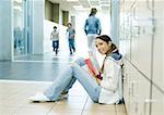Teen girl sitting on school hallway floor, leaning against lockers
