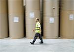 Factory worker walking past rolls of paper