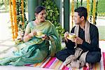 Young man and a mid adult woman sitting on a mat and holding cups of tea