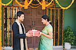 Side profile of a mid adult man giving a gift box to a young woman