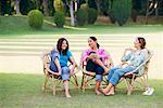 Three young women sitting on chairs in a park and smiling