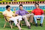 Three young men sitting on chairs at the poolside and smiling