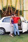 Portrait d'un jeune couple debout près de la porte ouverte d'une voiture et souriant