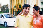 Close-up of a young couple standing in front of a decorated house and smiling