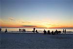 Gens sur la plage en regardant le coucher du soleil