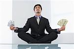 Businessman Meditating with American and European Currencies