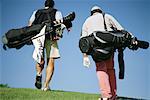 Golfers carrying golf bags, rear view