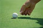 Golfer placing golf ball marker on turf, close-up of hand