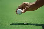 Golfer placing golf ball on turf, close-up of hand