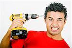 Portrait of a young man holding a drill machine against his head