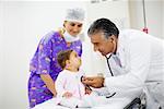 Side profile of a male doctor examining a baby girl with a stethoscope and a female doctor standing near them