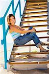 Portrait of a young woman sitting on a staircase of a lifeguard hut and smiling