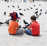 Rear view of two boys sitting with pigeons in front of them, Venice, Veneto, Italy