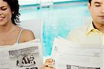 Close-up of a young couple reading newspapers at the poolside