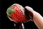 Gros plan de la main d'une personne détenant une fraise recouverte de chocolat